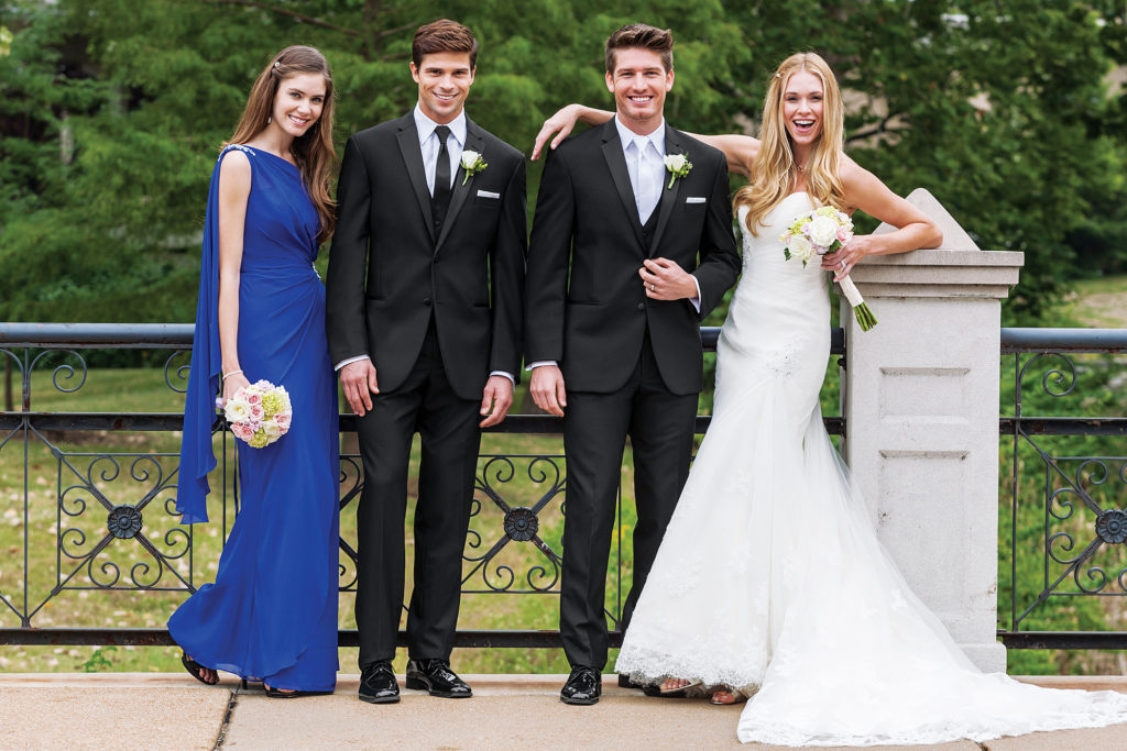 A wedding couple in elegant wedding suits, standing together. On both sides, a young boy and girl smiling happily